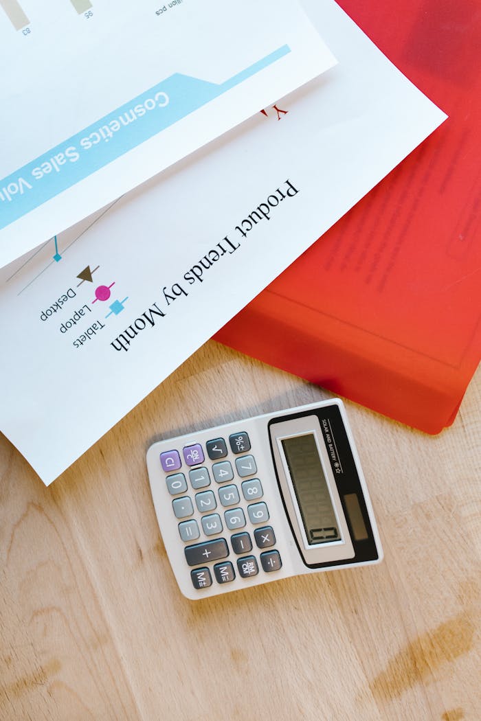 Calculator on desk with business documents and charts detailing product trends.